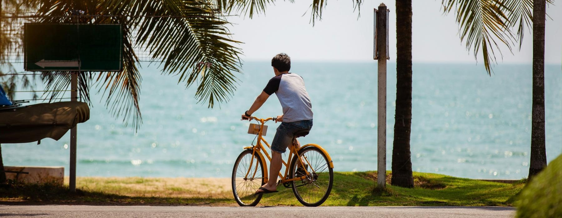 a man riding a bicycle on a road by a beach