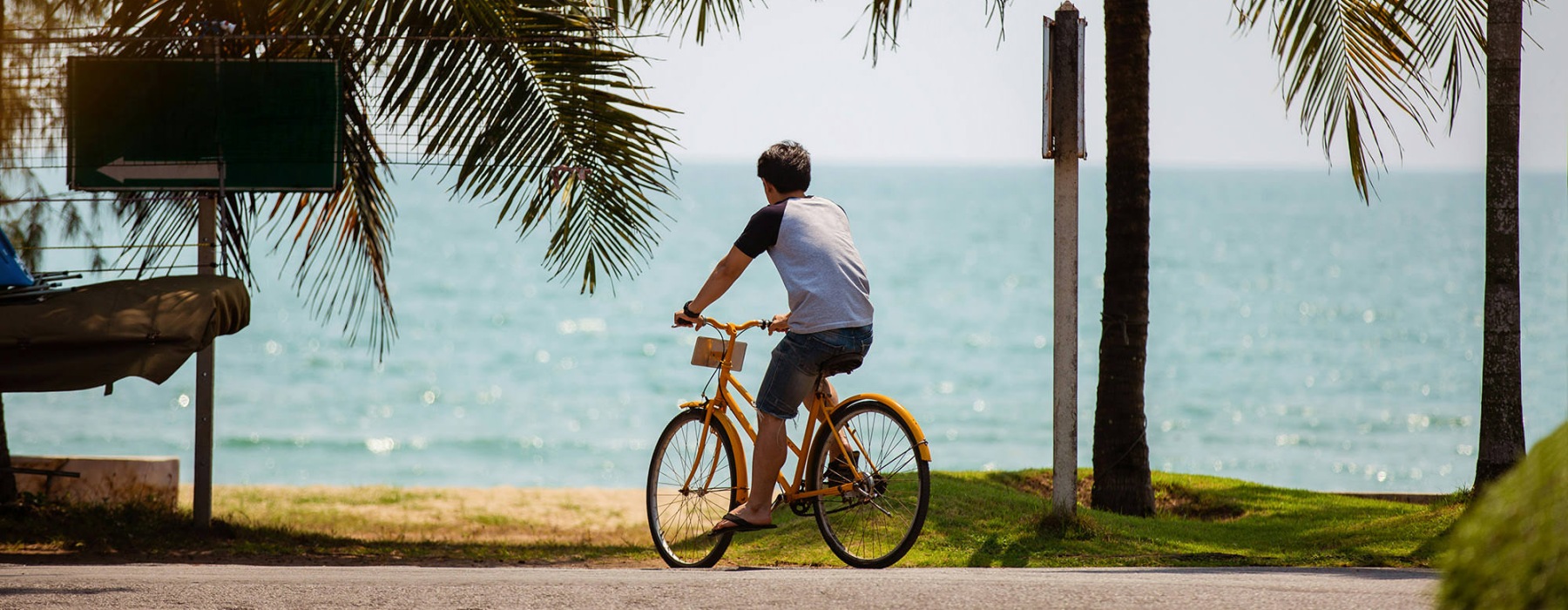 a man riding a bicycle on a road by a beach